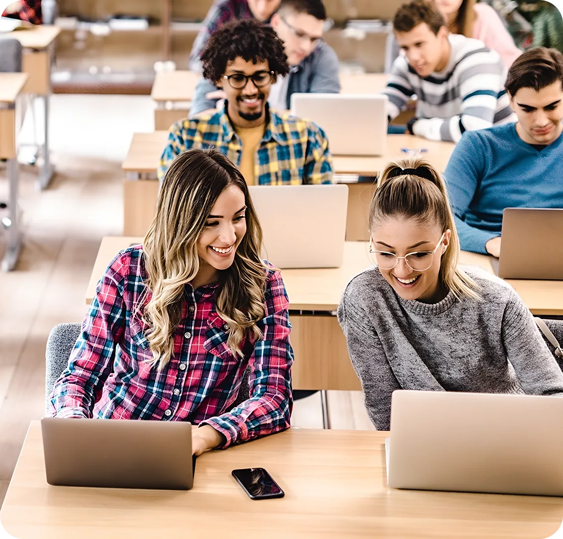 Étudiantes échangeant devant leurs ordinateurs en classe